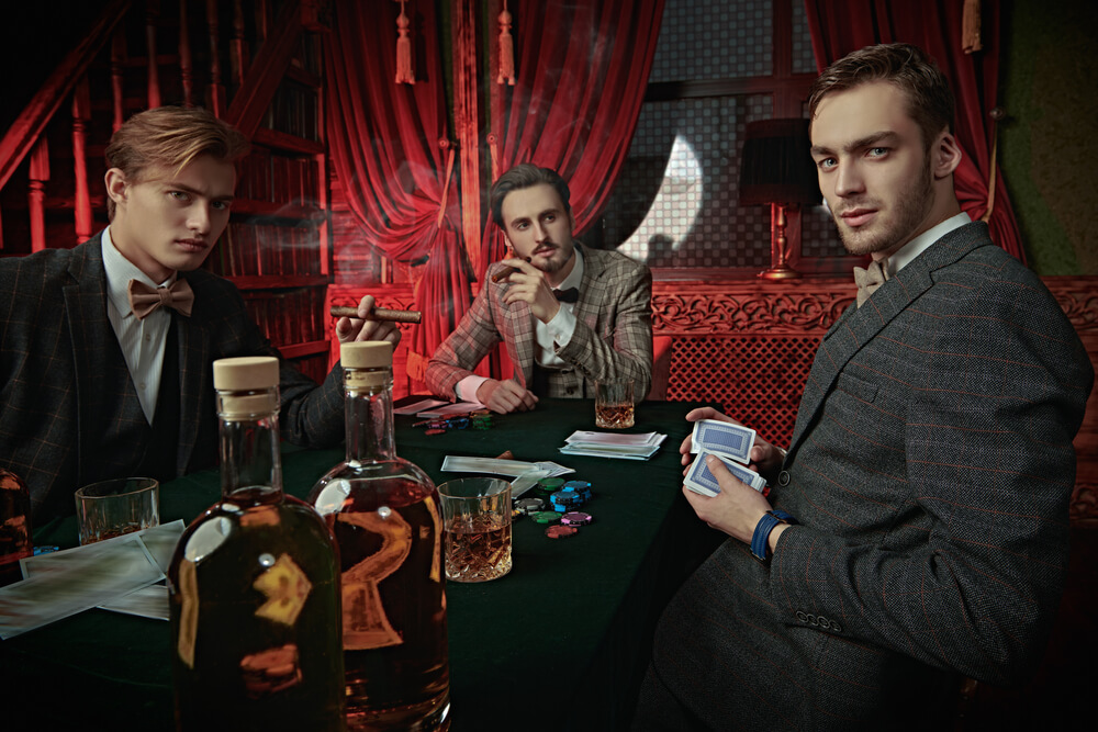 4 men playing poker in person with chips around them looking at the camera